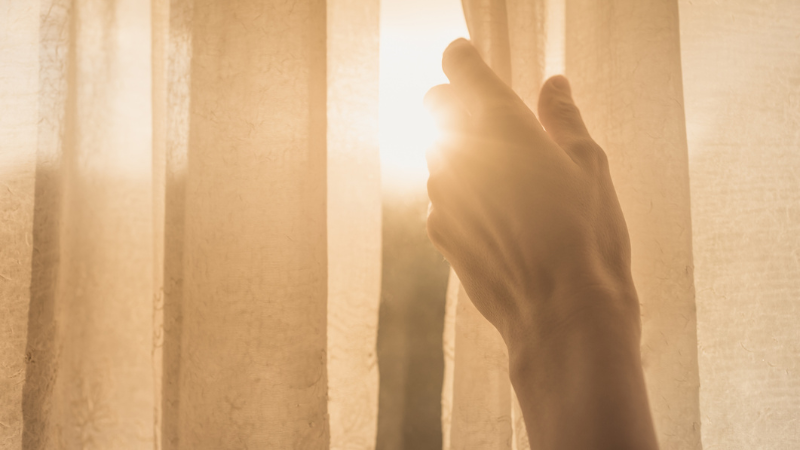 hand opening the curtain to let in the sun